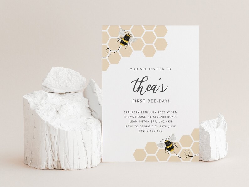 K&ouml;nnte beinhalten: Eine wei&szlig;e Karte mit einer bienenf&ouml;rmigen Einladung zu einer ersten Geburtstagsfeier. Die Karte hat ein Wabenmuster mit einer Biene auf jeder Seite. Der Text lautet "You are invited to Thea's First Bee-Day!" mit Datum, Uhrzeit und Ort der Party.