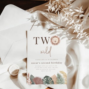 May include: A white invitation card with brown text that reads "TWO wild" with a lion illustration. The text below reads "Please join us to celebrate oscar's second birthday Saturday 15th July 2022 at 3PM 4 Elm Tree Close, Kent, LM2 4RQ RSVP to Jessie by 10th June 0208 123 175". The card is decorated with watercolor illustrations of tropical leaves.