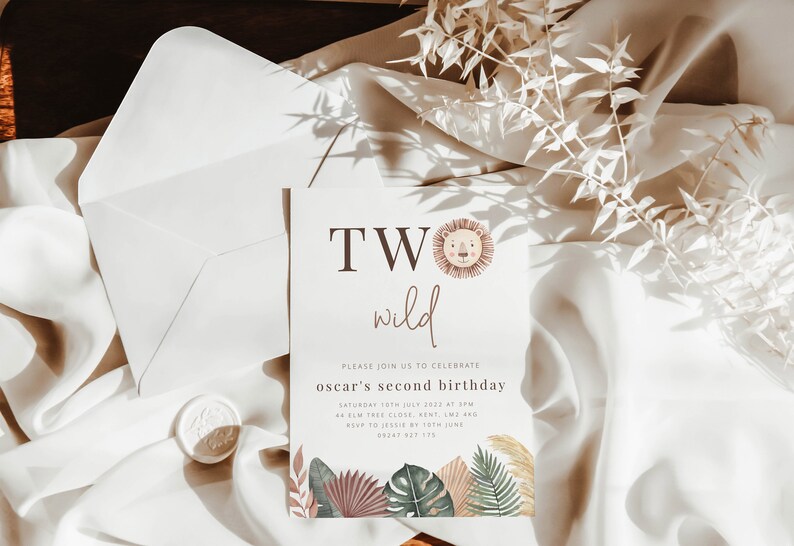 May include: A white invitation card with brown text that reads "TWO wild" with a lion illustration. The text below reads "Please join us to celebrate oscar's second birthday Saturday 15th July 2022 at 3PM 4 Elm Tree Close, Kent, LM2 4RQ RSVP to Jessie by 10th June 0208 123 175". The card is decorated with watercolor illustrations of tropical leaves.