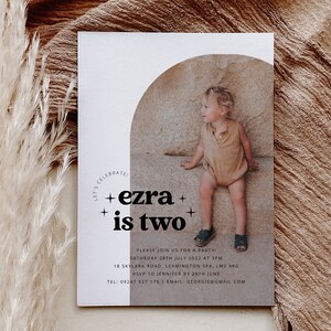 May include: A white and brown invitation card with a photo of a child sitting on a rock. The text on the card reads "Let's Celebrate! + ezra + is two + Please join us for a party! Saturday 28th July 2022 at 3pm 18 Skylark Road, Leamington Spa, LM2 4KG RSVP to Jennifer by 28th June Tel: 09247 927 175 Email: georgie@gmail.com"