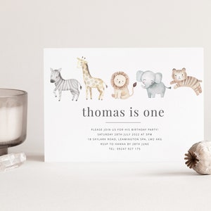 Pu&ograve; includere: Un invito bianco con una fila di animali ad acquerello, tra cui una zebra, una giraffa, un leone, un elefante e una tigre. Il testo sulla carta recita "thomas is one" e include i dettagli per una festa di compleanno.