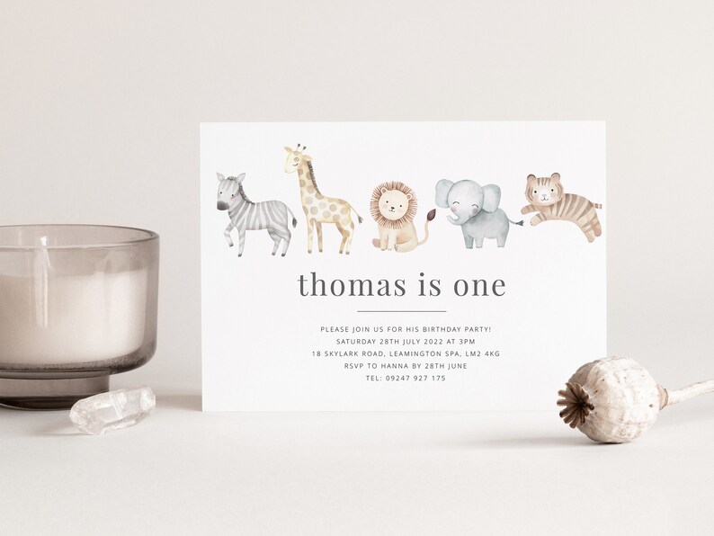 Pu&ograve; includere: Un invito bianco con una fila di animali ad acquerello, tra cui una zebra, una giraffa, un leone, un elefante e una tigre. Il testo sulla carta recita "thomas is one" e include i dettagli per una festa di compleanno.