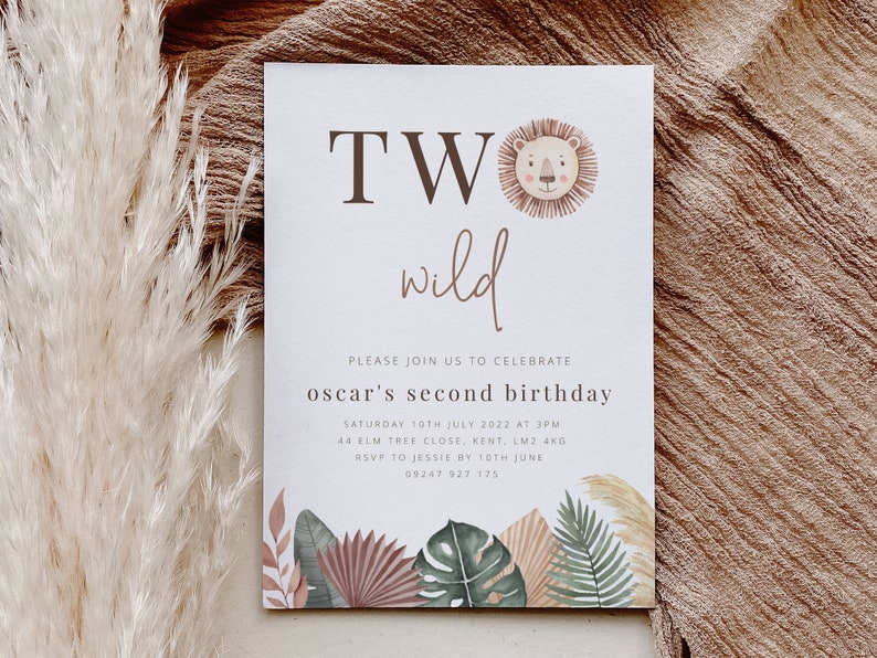 May include: A white invitation card with the text "TWO wild" in brown lettering. The card is decorated with a lion head illustration and tropical leaves. The text "Please join us to celebrate oscar's second birthday" is printed in brown lettering. The invitation includes the date, time, address, and RSVP information.