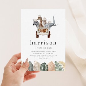 May include: A white invitation card with a safari theme. The card features a cartoon jeep with a zebra, giraffe, leopard, and elephant riding in it. The text on the card reads "harrison is turning one!" and includes details for a birthday party.