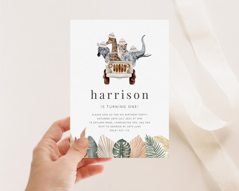 May include: A white invitation card with a safari theme. The card features a cartoon jeep with a zebra, giraffe, leopard, and elephant riding in it. The text on the card reads "harrison is turning one!" and includes details for a birthday party.
