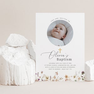 May include: A white baptism invitation with a gold cross and the text "Olivia's Baptism". The invitation features a photo of a baby in a white onesie and a floral border.
