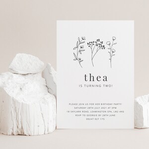 May include: A black and white birthday invitation for a child named Thea turning two. The invitation features a simple floral design and the text "thea is turning two!"  Please join us for her birthday party! Saturday 28th July 2021 at 3pm 18 Skylark Road, Leamington Spa, LM2 4KG RSVP to Georgie by 28th June 09247 927 175
