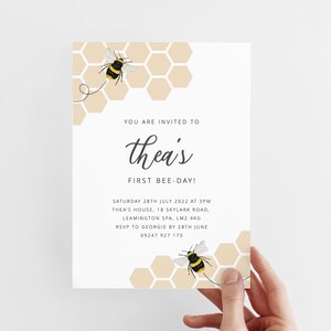 K&ouml;nnte beinhalten: Eine wei&szlig;e Einladungskarte mit einem Bienen-Motiv. Die Karte hat ein Wabenmuster mit zwei Bienen, die herumfliegen. Der Text auf der Karte lautet "You are invited to Thea's First Bee-Day!" Samstag, 28. Juli 2022 um 15:00 Uhr Thea's House, 18 Skylark Road, Leamington Spa, LM2 4KG RSVP an Georgie bis zum 28. Juni 09247 927 175