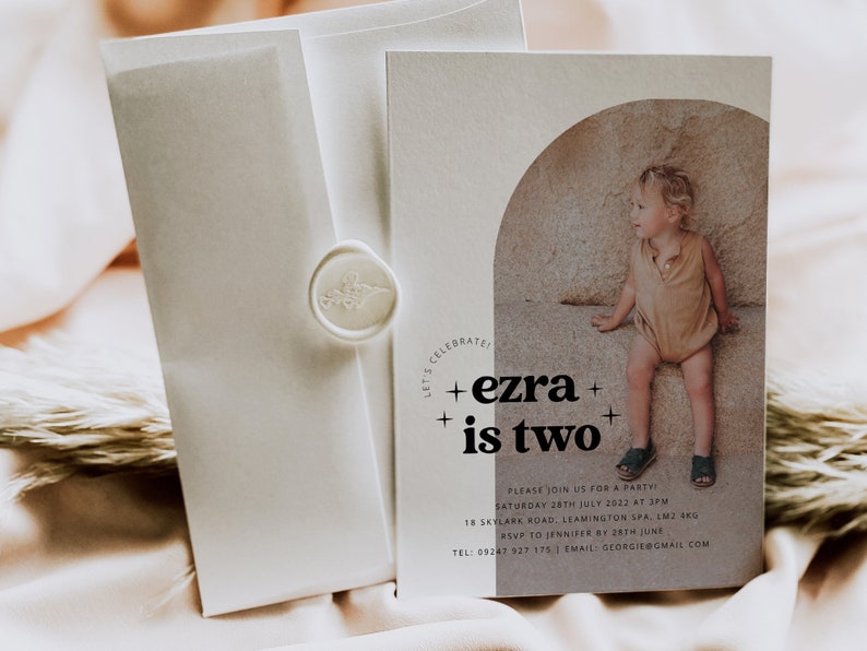 May include: A beige invitation card with a photo of a young boy sitting on a rock. The text on the card reads "CELEBRATE! +ezra+ +is two+" and includes details for a party.