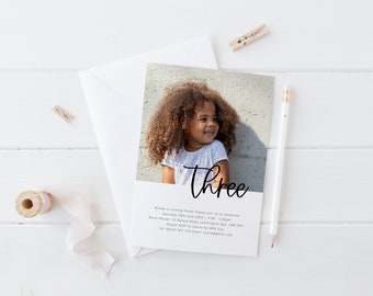 Op de afbeelding: Een verjaardagsuitnodiging met een foto van een jong meisje met krullend haar. De uitnodiging zegt "drie" in een zwart handschrift en bevat details over het verjaardagsfeest.