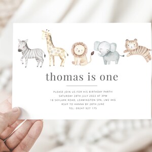 Pu&ograve; includere: Un invito bianco con un'illustrazione ad acquerello di una zebra, una giraffa, un leone, un elefante e una tigre. Il testo "thomas is one" &egrave; stampato in grigio nella parte superiore della carta. L'invito indica la data, l'ora, il luogo e le informazioni RSVP per una festa di compleanno.
