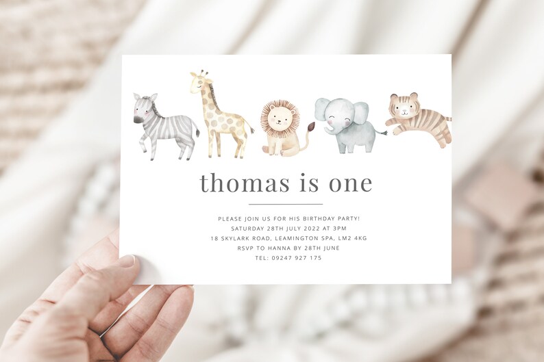 Pu&ograve; includere: Un invito bianco con un'illustrazione ad acquerello di una zebra, una giraffa, un leone, un elefante e una tigre. Il testo "thomas is one" &egrave; stampato in grigio nella parte superiore della carta. L'invito indica la data, l'ora, il luogo e le informazioni RSVP per una festa di compleanno.
