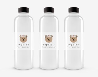 May include: Three clear plastic water bottles with labels that say "sophia's first birthday" and feature a cartoon bear wearing a floral crown.