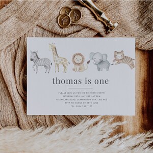 Pu&ograve; includere: Un invito bianco con un'illustrazione ad acquerello di una zebra, una giraffa, un leone, un elefante e una tigre. Il testo "thomas is one" &egrave; stampato in grigio nella parte superiore della carta. L'invito indica la data, l'ora e il luogo di una festa di compleanno.