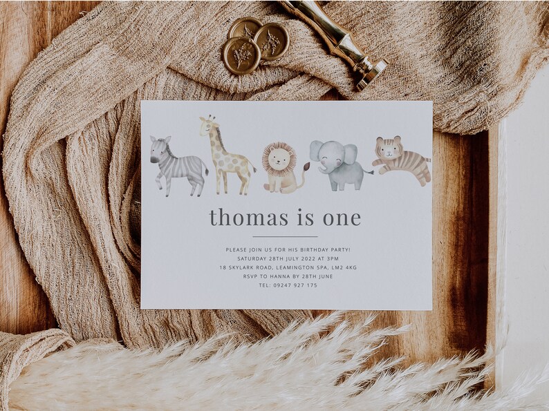 Pu&ograve; includere: Un invito bianco con un'illustrazione ad acquerello di una zebra, una giraffa, un leone, un elefante e una tigre. Il testo "thomas is one" &egrave; stampato in grigio nella parte superiore della carta. L'invito indica la data, l'ora e il luogo di una festa di compleanno.