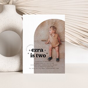 May include: A white invitation with a photo of a child sitting on a rock. The invitation says "Let's Celebrate + ezra + is two +" and includes details for a birthday party.