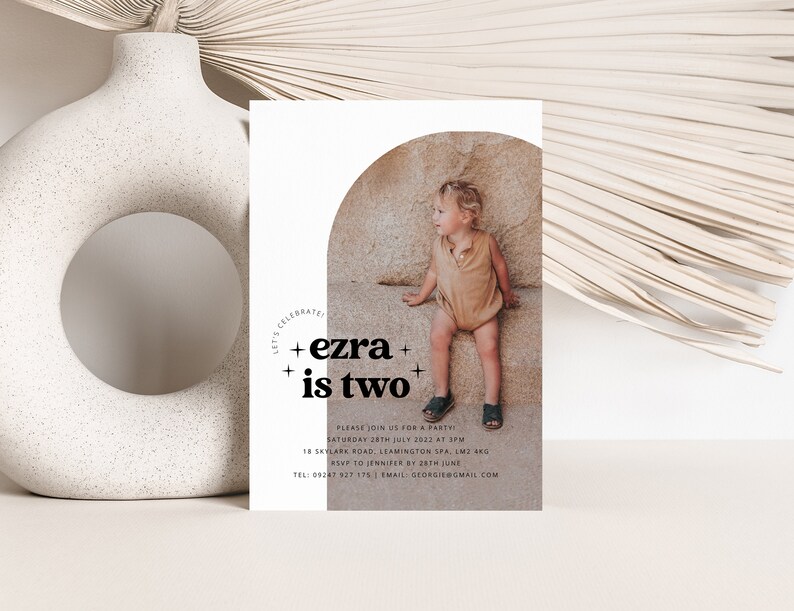 May include: A white invitation with a photo of a child sitting on a rock. The invitation says "Let's Celebrate + ezra + is two +" and includes details for a birthday party.