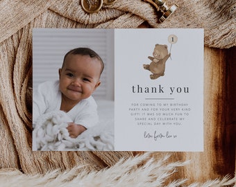 Pode incluir: Um cartão de agradecimento com fundo azul claro que apresenta uma ilustração de desenho animado de um urso marrom segurando um balão com o número "1" nele. O texto "thank you" está impresso em preto com uma linha abaixo. O texto "FOR COMING TO MY BIRTHDAY PARTY AND FOR YOUR VERY KIND GIFT! IT WAS SO MUCH FUN TO SHARE AND CELEBRATE MY SPECIAL DAY WITH YOU. love from lea xo" está impresso em preto abaixo da ilustração.