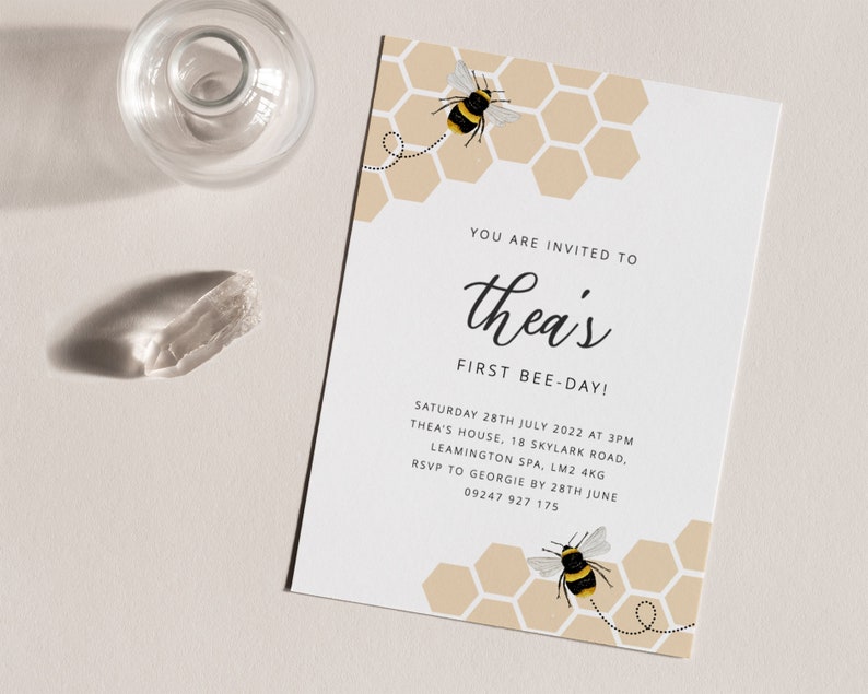 K&ouml;nnte beinhalten: Eine Einladung zu einer ersten Geburtstagsfeier zum Thema Bienen mit einem Wabenmuster und zwei Comic-Bienen. Der Text der Einladung lautet "You are invited to Thea's First Bee-Day!" mit Datum, Uhrzeit und Ortsangaben darunter.