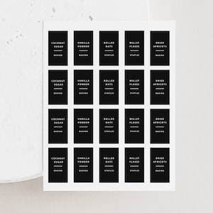 Peut inclure: Une feuille de 20 étiquettes noires et blanches avec du texte blanc. Les étiquettes sont destinées à l'organisation du garde-manger et comprennent des catégories telles que "Cuisson" et "Aliments de base". Les étiquettes comprennent les éléments suivants : sucre de coco, poudre de vanille, flocons d'avoine, flocons de millet et abricots secs.