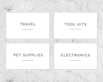 May include: Four white rectangular labels with black borders and text on a white marble background. The labels are arranged in two rows of two. The top left label says "TRAVEL", the top right label says "TOOL KITS", the bottom left label says "PET SUPPLIES", and the bottom right label says "ELECTRONICS".