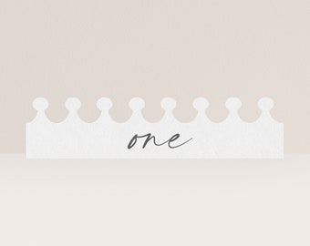 Op de afbeelding: Witte papieren kroon met het woord "one" in zwarte cursieve letters.