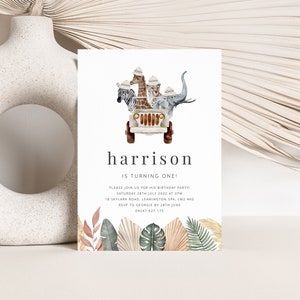 May include: A white invitation card with a jungle theme. The card features a cartoon jeep with a giraffe, zebra, lion, and elephant riding in it. The text on the card reads "harrison is turning one!" and includes details for a birthday party.