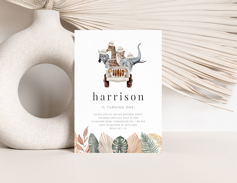 May include: A white invitation card with a jungle theme. The card features a cartoon jeep with a giraffe, zebra, lion, and elephant riding in it. The text on the card reads "harrison is turning one!" and includes details for a birthday party.