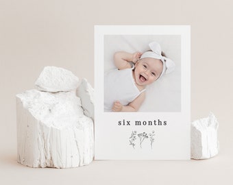 May include: A white card with a photo of a baby girl smiling. The card says "six months" and has a small floral design.