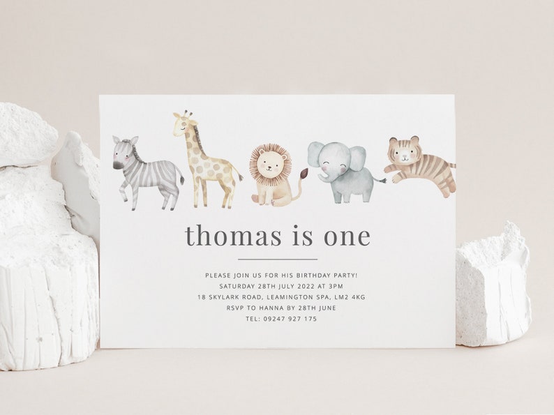 Pu&ograve; includere: Un invito bianco con una fila di animali ad acquerello, tra cui una zebra, una giraffa, un leone, un elefante e una tigre. Il testo "thomas is one" &egrave; stampato in nero nella parte superiore della carta. I dettagli dell'invito sono stampati in nero sotto gli animali.