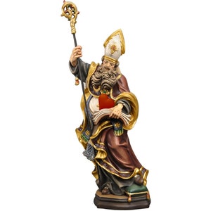 Op de afbeelding: Gedetailleerd houten beeld van een religieuze figuur, gekleed in een lange bordeauxrode jurk met gouden randen en een witte en gouden hoed. De figuur houdt een staf in één hand en een boek en een hart in de andere. Het beeld staat op een donkere basis.