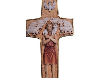 May include: A wooden cross with a carved image of Jesus as the Good Shepherd carrying a lamb. The cross is decorated with a dove at the top and a flock of sheep surrounding Jesus.
