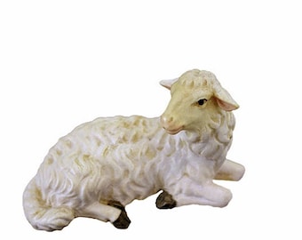 May include: A white ceramic sheep figurine lying down with its head turned to the side. The sheep has a light brown face and black hooves.