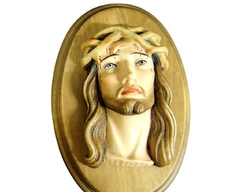 Könnte beinhalten: Eine ovale Holzplakette mit einem geschnitzten Bild von Jesus Christus. Das Bild ist in realistischen Farben gemalt und zeigt Jesus mit einer Dornenkrone und einem traurigen Ausdruck.