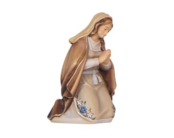 May include: A wooden figurine of Mary kneeling in prayer, wearing a brown robe with a white undergarment and floral accents.