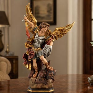 May include: A detailed figurine of Archangel Michael depicted with large golden wings, wearing silver armour and a flowing red cloak. The figure holds a sword aloft and a shield, standing over a dark, defeated demonic figure on a rocky base.