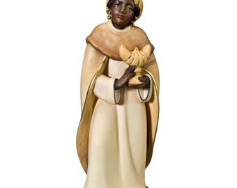 May include: A wooden figurine of a king, dressed in a white robe with a gold trim, a brown cloak, and a gold crown. He has dark skin, brown eyes, and is holding a golden chalice.