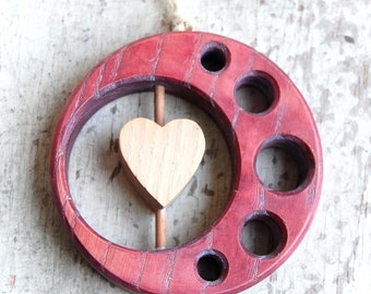 May include: A red wooden crescent moon with a small wooden heart hanging from a dowel rod inside the moon. The moon has six holes around the edge.