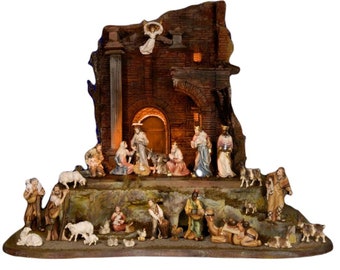 May include: A detailed nativity scene set with a brown stone building, a manger, and figures of Mary, Joseph, baby Jesus, angels, shepherds, and animals. The scene is lit with warm white lights.