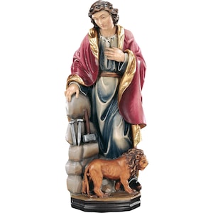 Puede incluir: Una estatua de madera de un santo con una túnica roja y dorada, sosteniendo un martillo y clavos. El santo está de pie sobre una base de piedra con un león a sus pies.