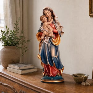Könnte beinhalten: Eine handbemalte Statue einer Frau in einem fließenden blau-rot-goldenen Gewand, die ein kleines Kind hält. Die Figur steht auf einem runden Sockel und zeigt detaillierte Gesichtszüge sowie kunstvoll drapierte Stofffalten.