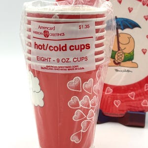 May include: A stack of eight red paper cups, each holding 9 oz, with white stripes and heart designs. The cups are packaged in clear plastic and labeled "hot/cold cups" by American Greetings.
