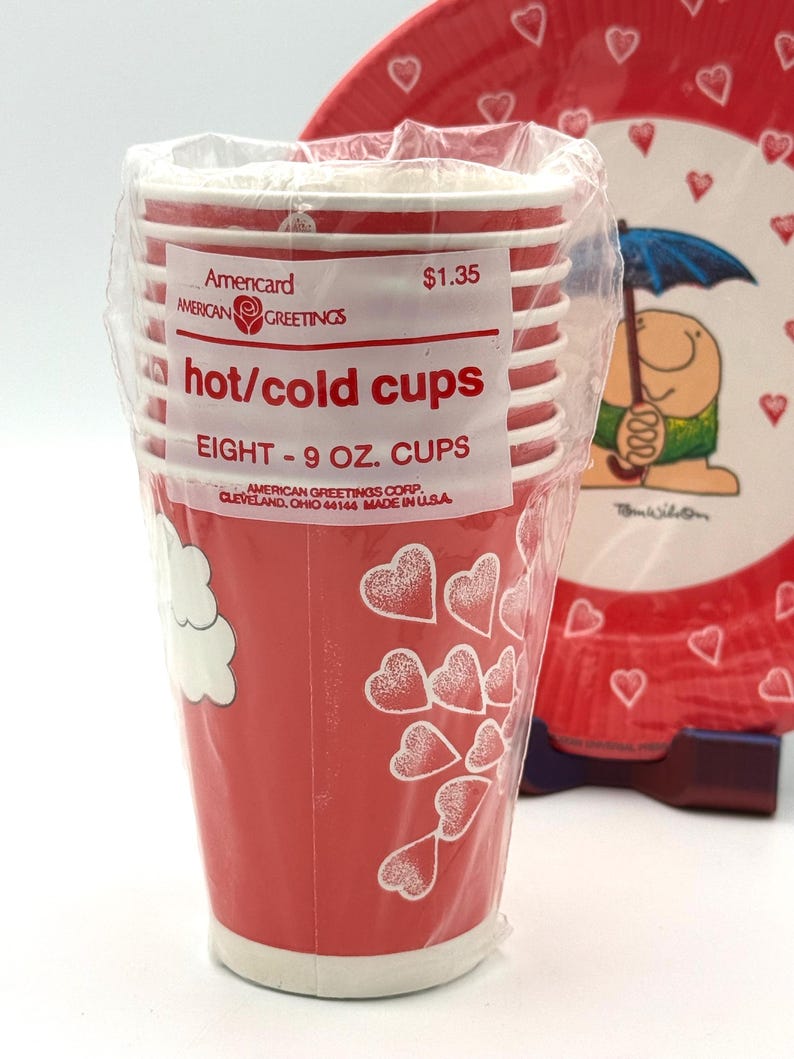 May include: A stack of eight red paper cups, each holding 9 oz, with white stripes and heart designs. The cups are packaged in clear plastic and labeled "hot/cold cups" by American Greetings.