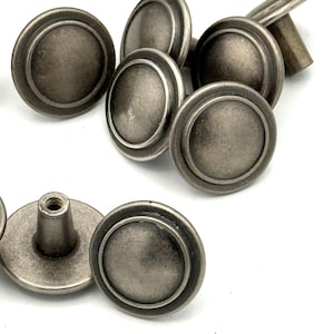 May include: A collection of round metal knobs with a weathered silver finish. Each knob features a smooth, slightly domed circular face with a raised outer rim and a central threaded post on the back for attachment, showing a consistent industrial design.