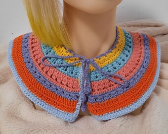May include: A rainbow-striped crochet collar featuring shades of orange, pink, yellow, blue, and purple. The collar is secured with a lavender tie. This handmade accessory adds a vibrant touch to any outfit.