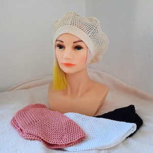 May include: Three crocheted hats in different colors: pink, white, and black. The hats are made with a loose, open stitch and have a rounded shape.