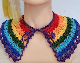 May include: A vibrant, rainbow-hued crochet collar with a scalloped edge and a purple tie. The collar showcases a spectrum of colours: red, orange, yellow, green, blue, and purple. The collar is displayed on a mannequin.