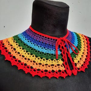 May include: A rainbow crochet collar with a red tie closure. The collar is made of a variety of colors, including red, orange, yellow, green, blue, indigo, and violet.