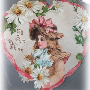 Può includere: Un biglietto di San Valentino vintage con una bambina con un berretto rosa che tiene un mazzo di margherite bianche. Il biglietto è a forma di cuore e ha un bordo rosa. Il testo sul biglietto dice "All Joys be Thine".