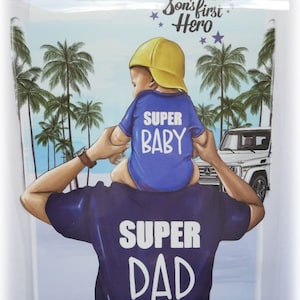 May include: A father and son are standing in front of a beach scene. The father is wearing a blue shirt that says "Super Dad" and the son is wearing a blue shirt that says "Super Baby". The son is sitting on the father's shoulders. The text "A Father is his Son's First Hero" is written in the top right corner of the image.